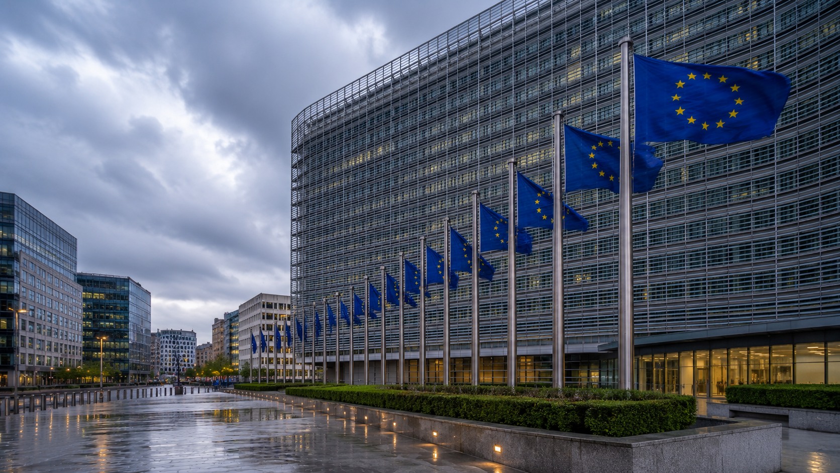 Row of European Union flags before the curved glass Berlaymont building under an overcast sky with wet reflective pavement